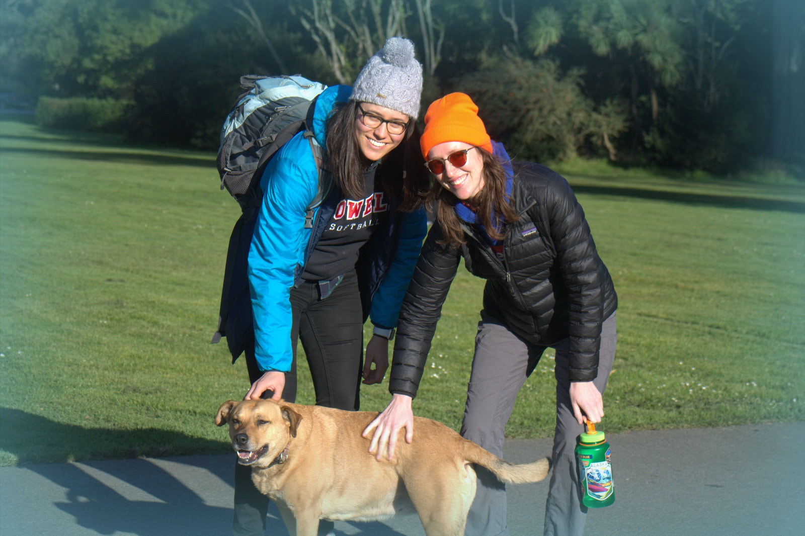 Stella and Friends — two women in winter jackets bending down to pet Stella in the park